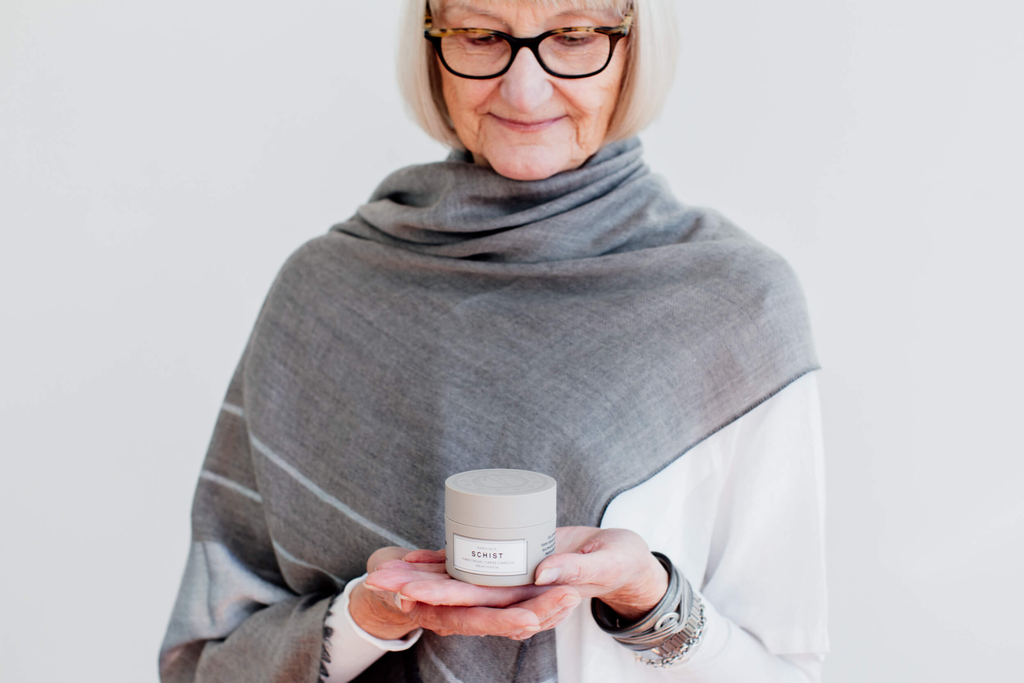 Older woman with grey hair holding a styling cream by Maria Nila.