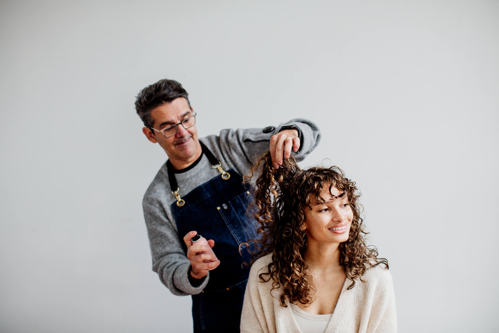Hairstylist is spraying on styling spray on a customer with curly hair. 