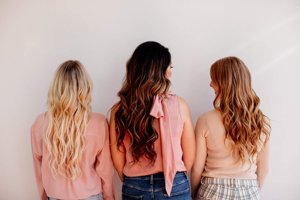 Three woman showing their hair extensions, blonde, brunette, and red hair. 