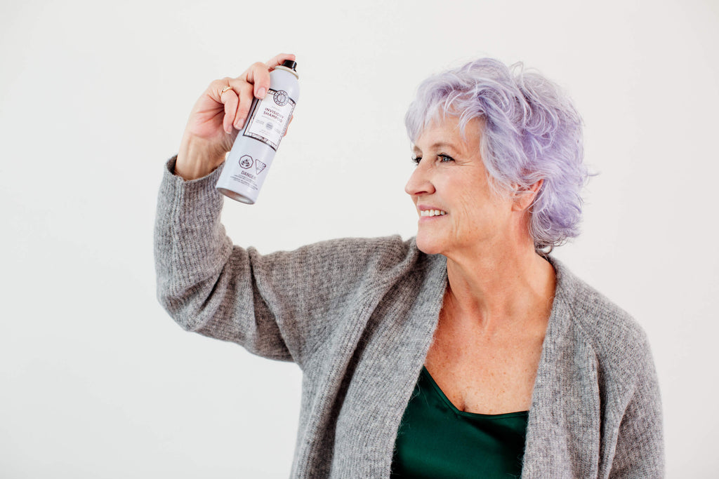 Woman is with silver hair is holding a bottle of Maria Nila hair product for grey hair.