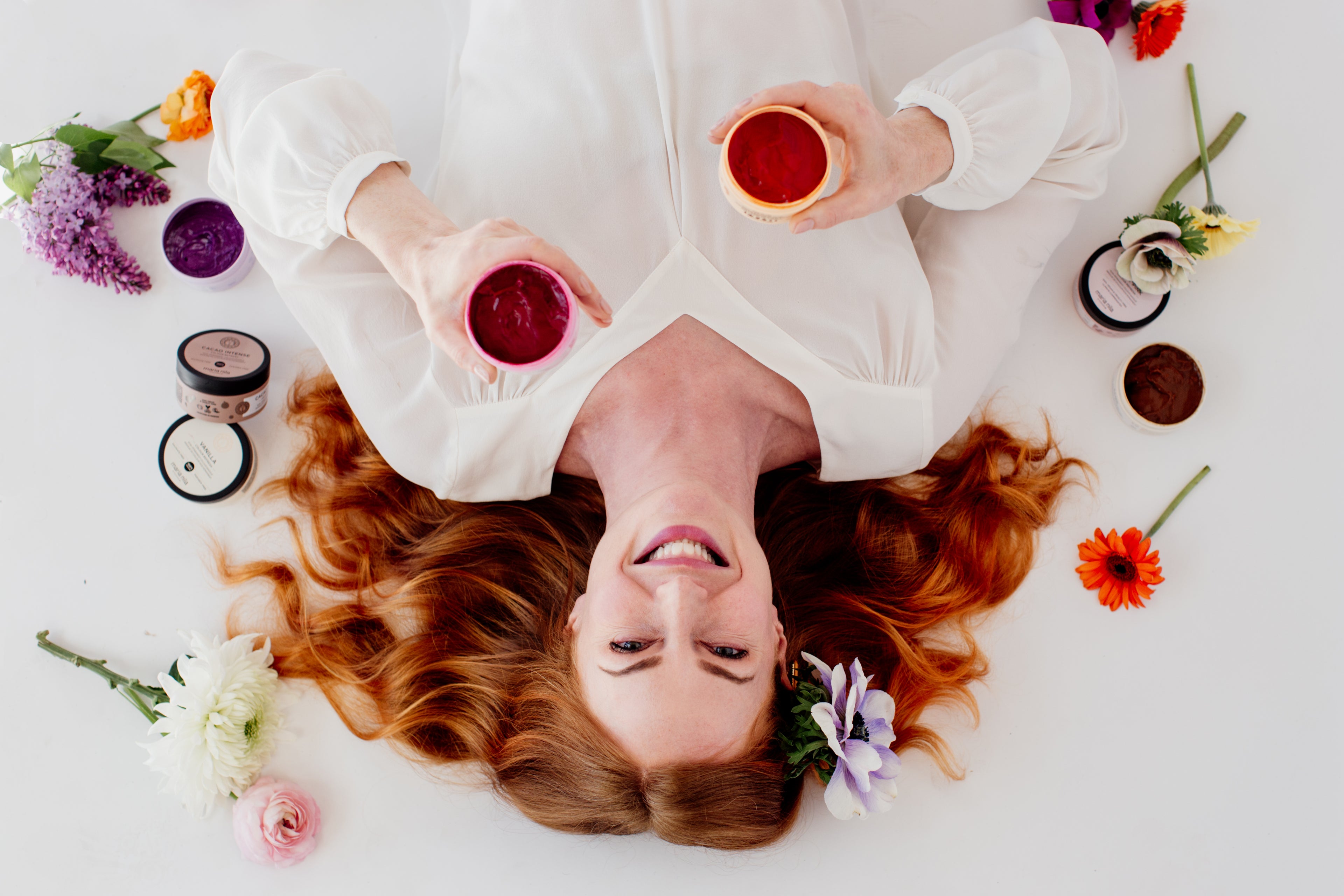 Woman looking up smiling, she is surrounded by Maria Nila hair products and flowers.