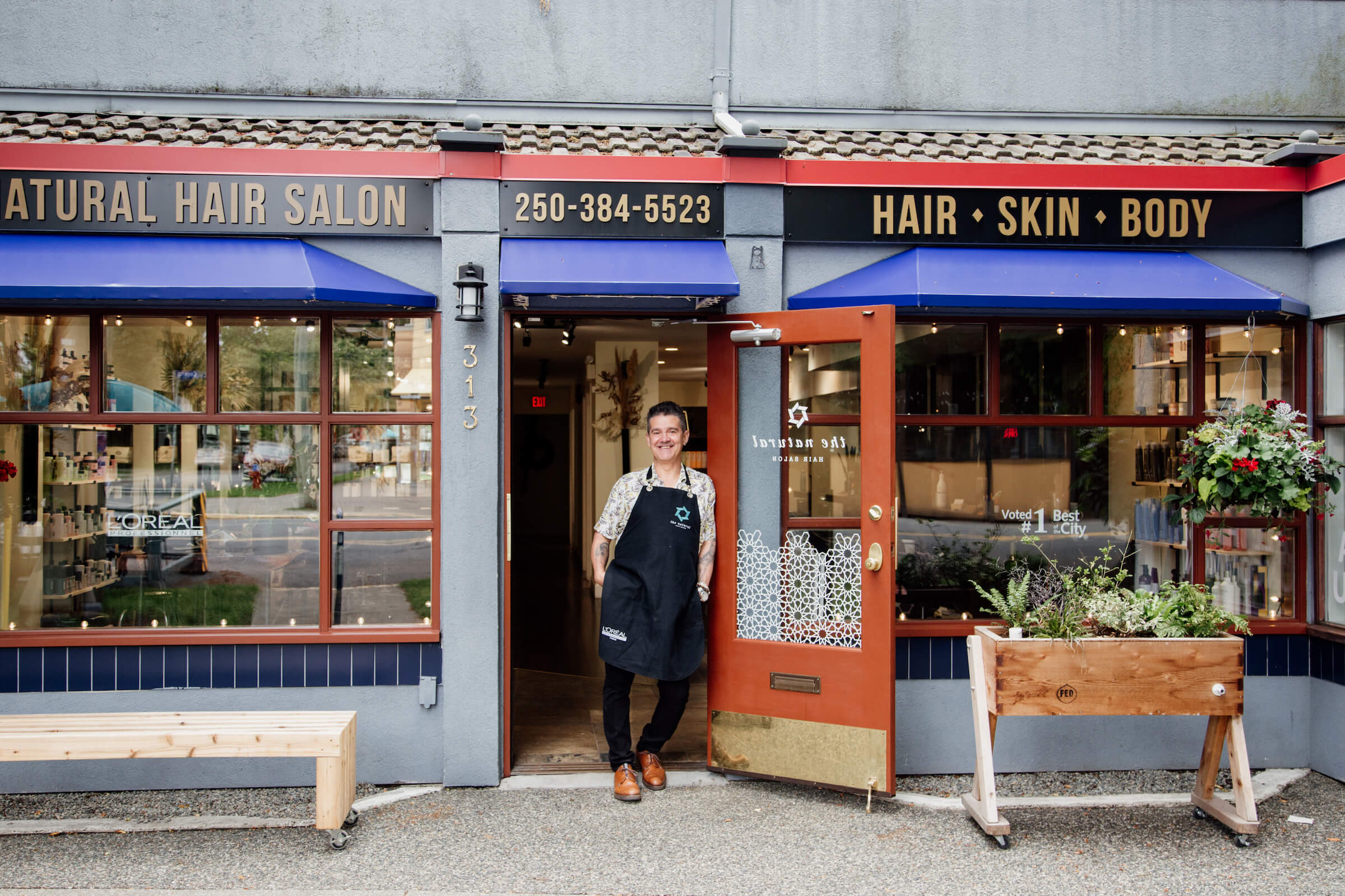 A ahirdresser stands outside his salon and smiles.